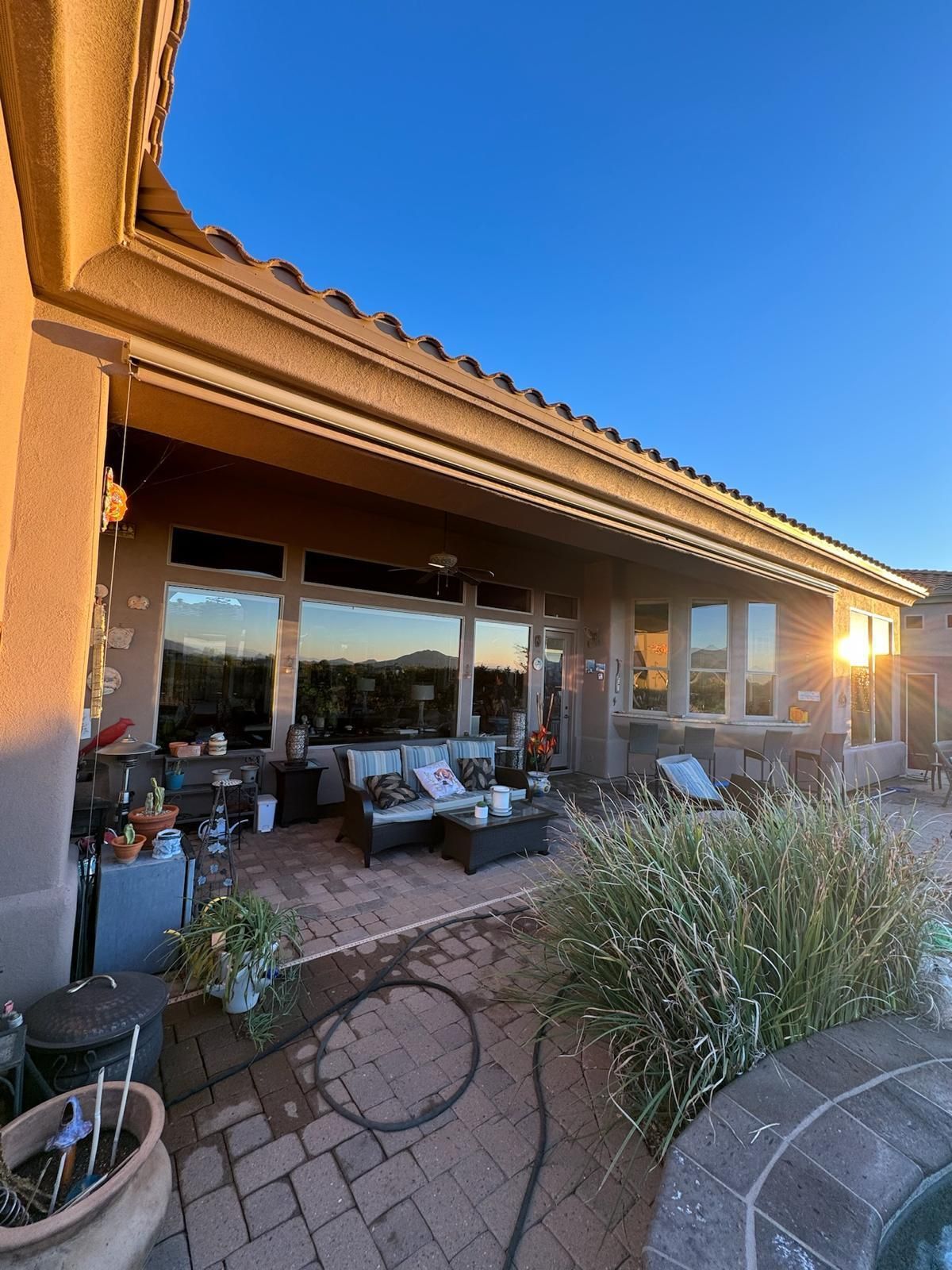 Patio with outdoor seating and potted plants beside a stucco house at sunset