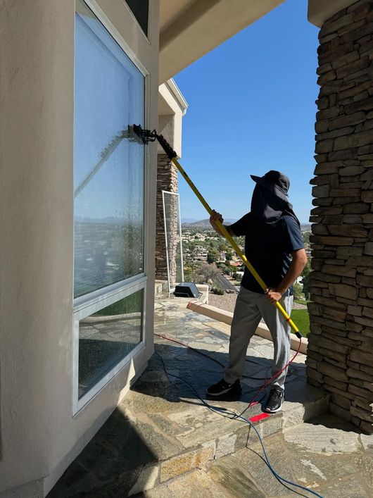 Person cleaning a second-story window with a long pole on an outdoor stone patio