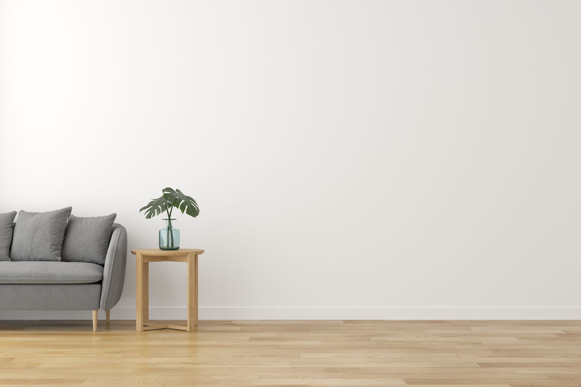 Gray couch, wooden side table with plant, against a white wall and wood floor.