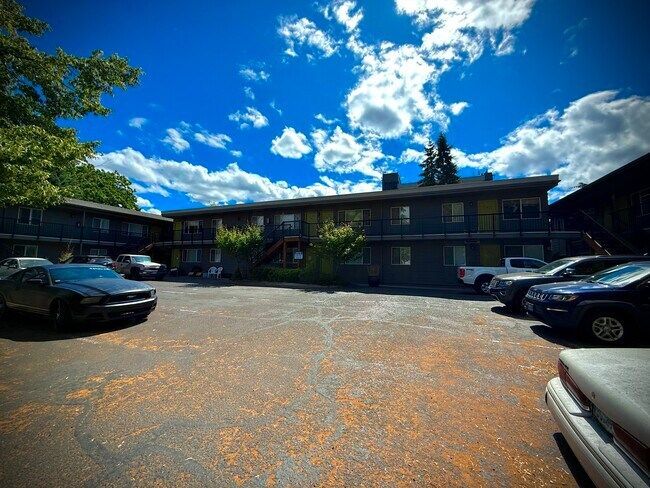 Apartment building with cars parked outside on a sunny day with blue sky and white clouds.