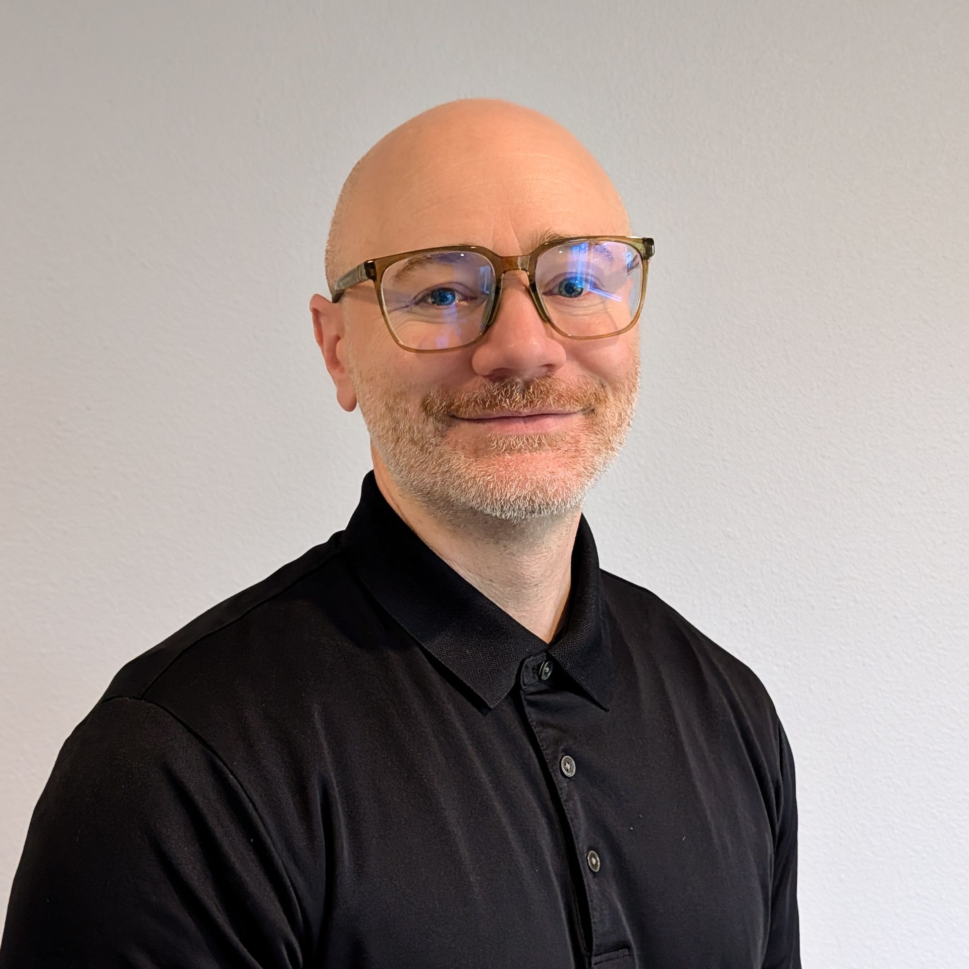 Smiling bald man wearing glasses and a black shirt against a plain light-gray background