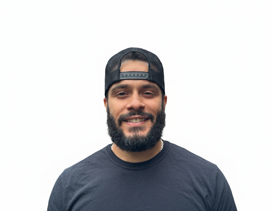 Man with a full beard wearing a black cap and t-shirt smiling against a white backdrop.