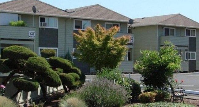 Two-story apartment complex with green siding, brown roof, and landscaped garden.