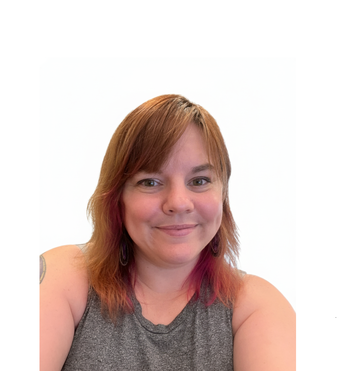 Woman with auburn hair and pink highlights smiling; wearing a gray tank top against a white backdrop.