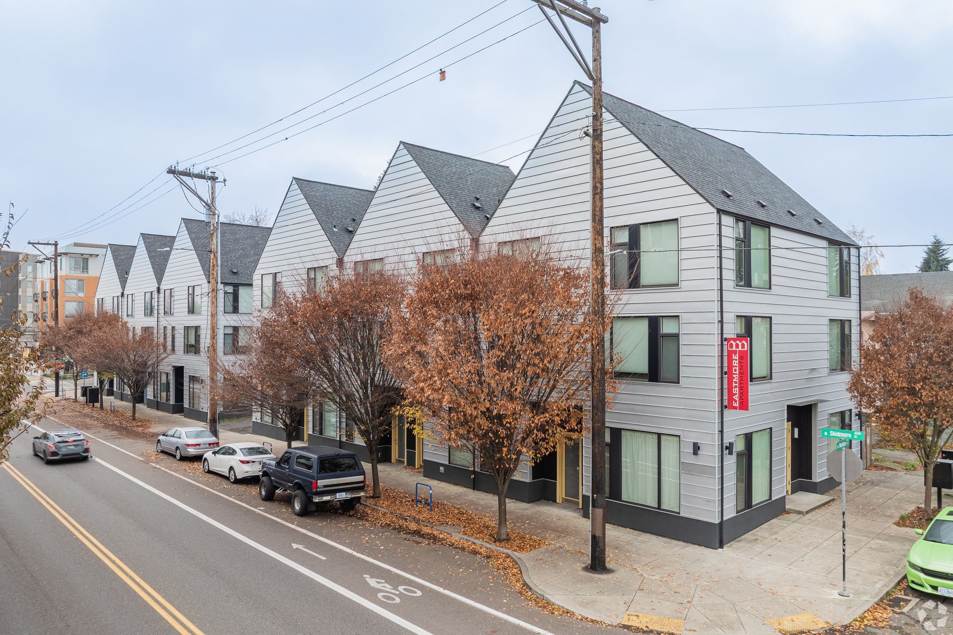 Row of modern gray townhouses with gabled roofs along a city street. Cars parked on the side.