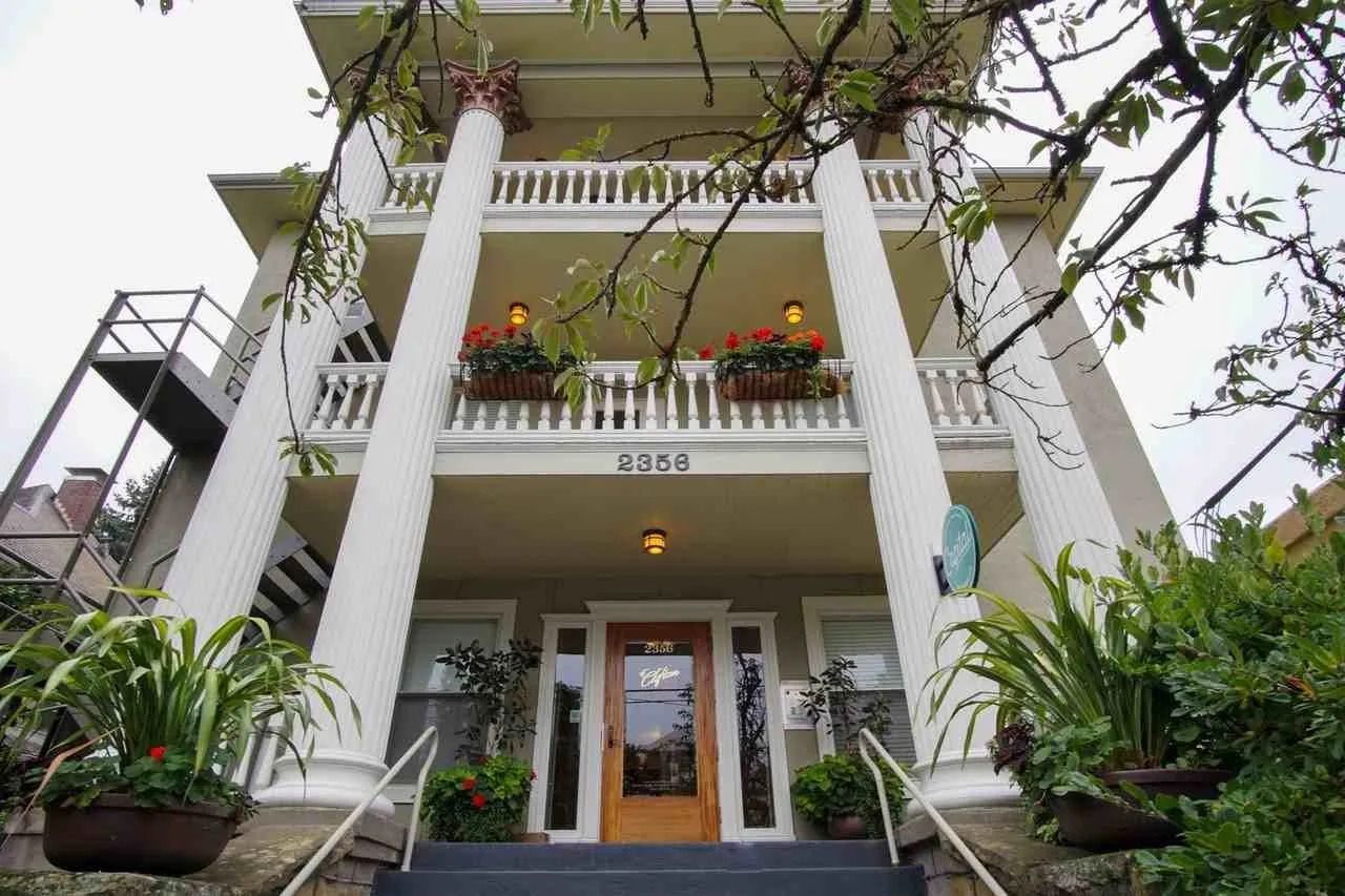 Three-story building with white columns and balcony planters; exterior staircase to the left.