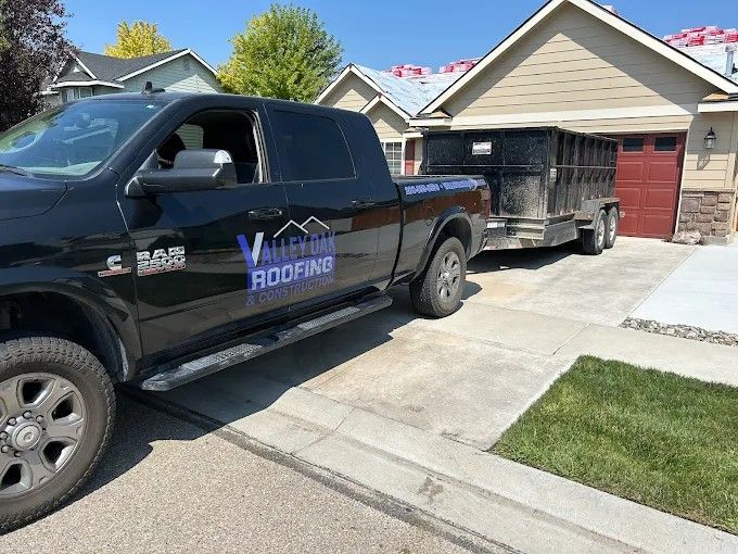 Black roofing truck with trailer parked in a suburban driveway next to a red garage.