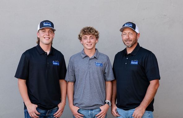 Three people in branded polo shirts standing against a plain wall, smiling at the camera.