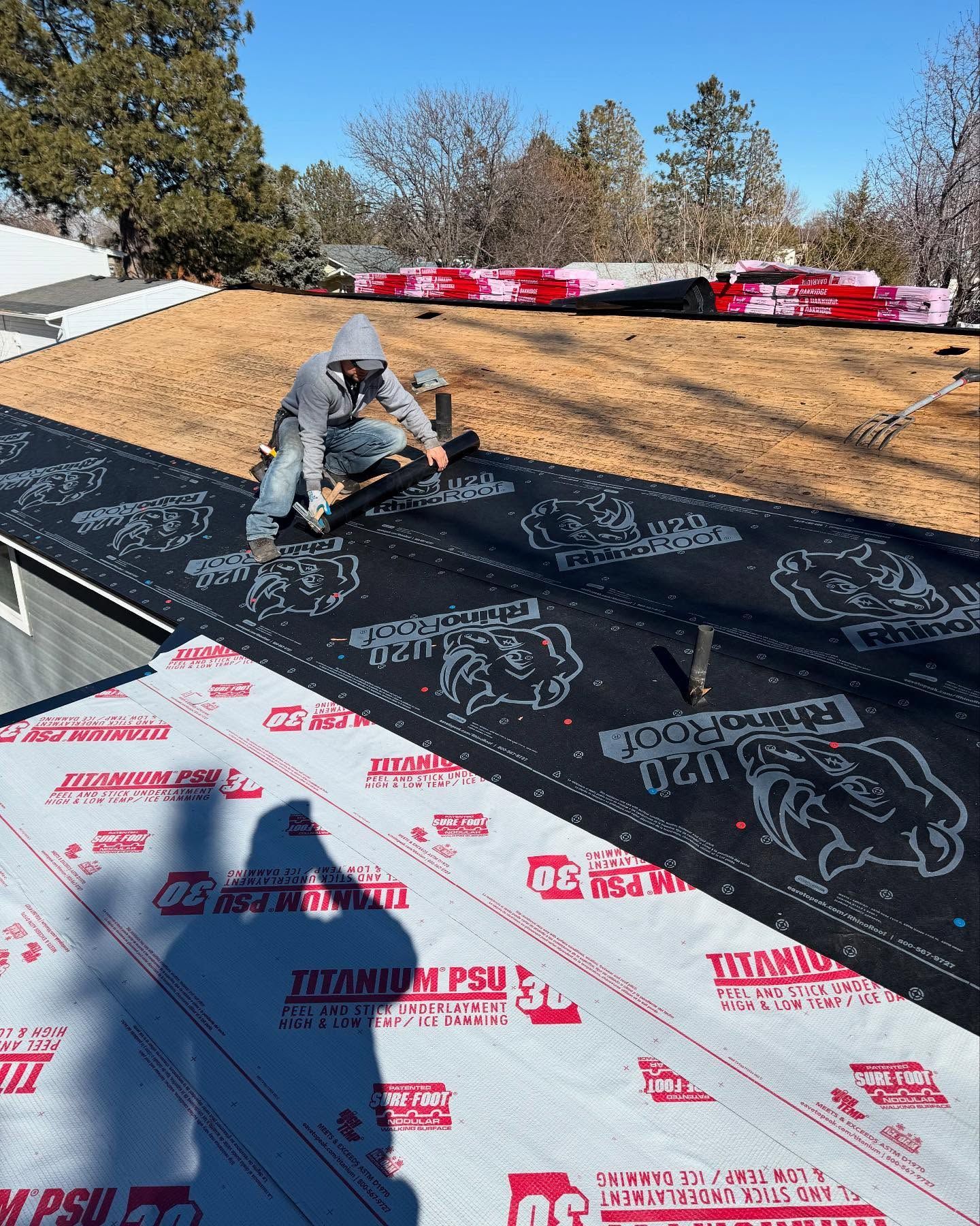Worker installing roofing underlayment on a steep roof, with black and white protective sheets visible.