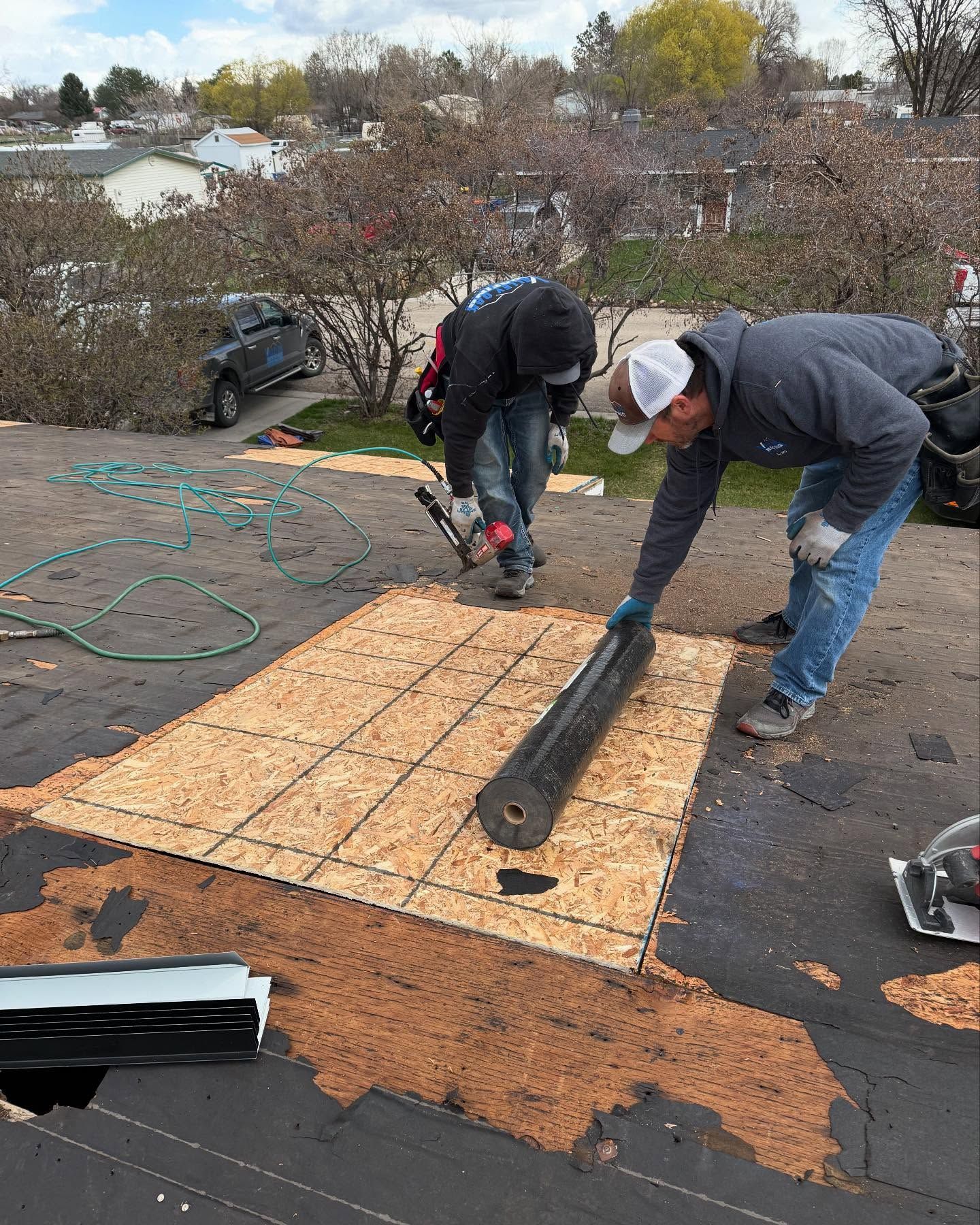 Two workers installing roofing felt on a house roof on a cloudy day