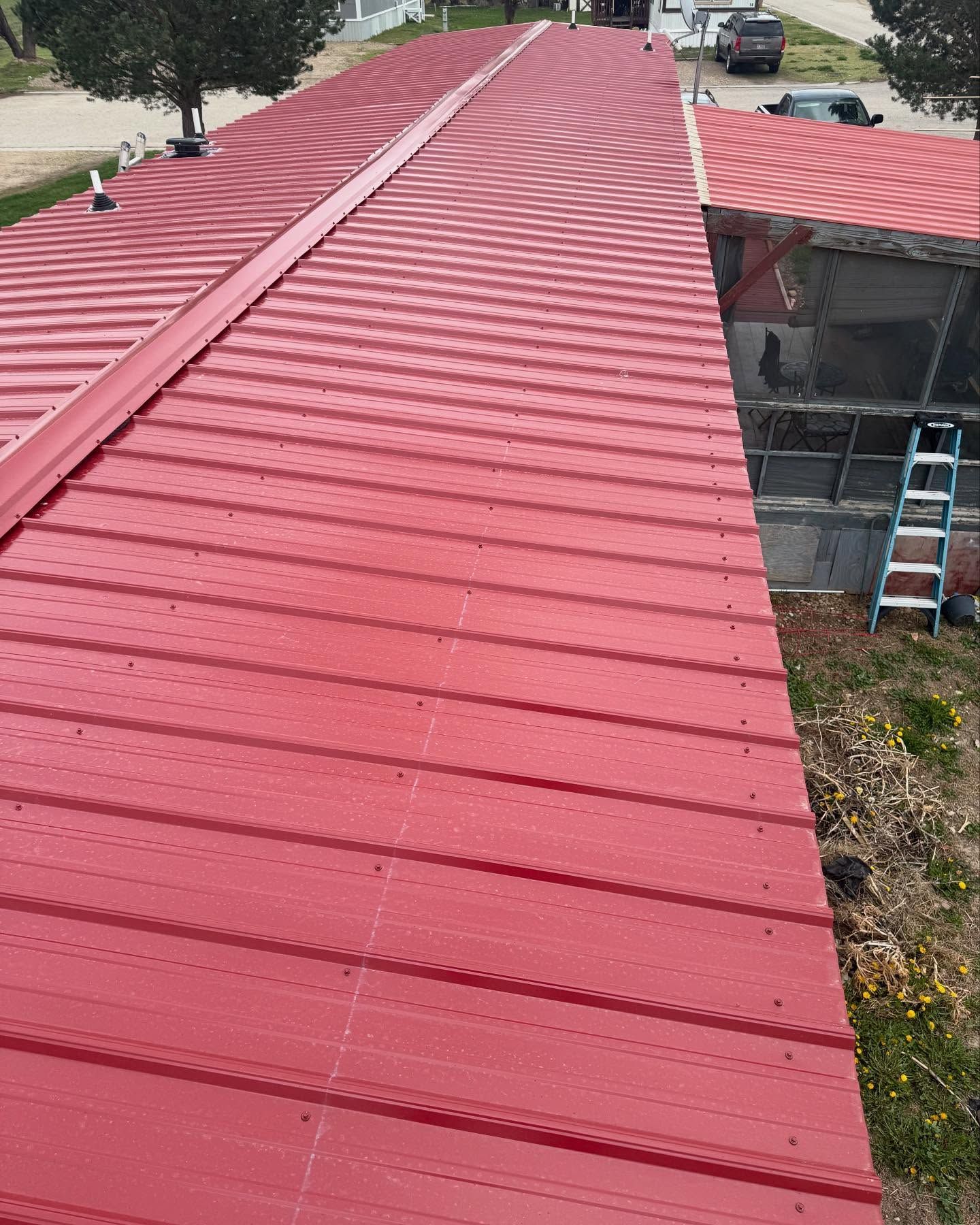 Red metal roof on a house, viewed from above with a ladder at the side.
