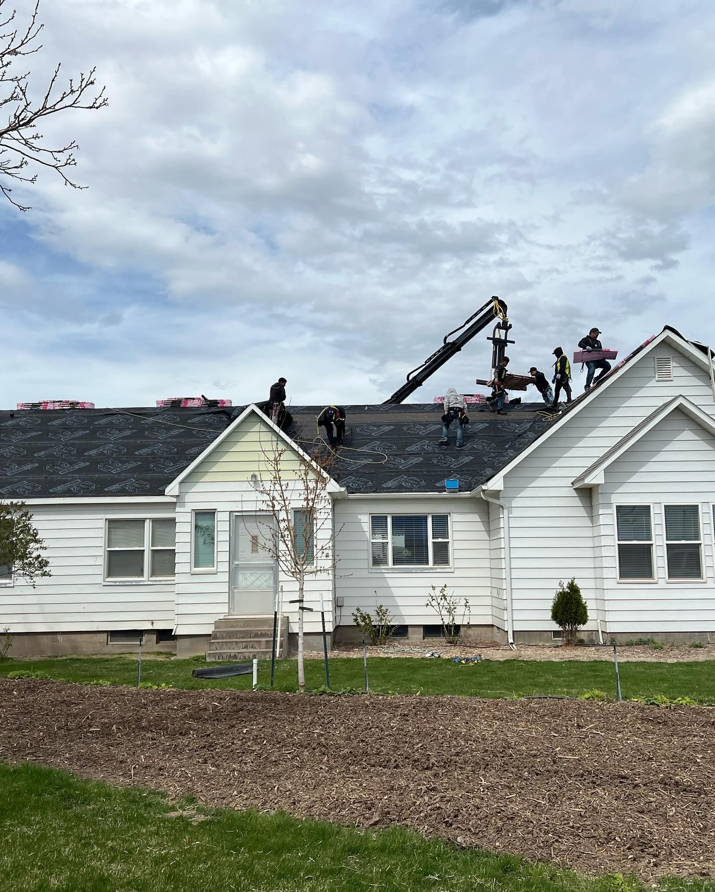 Workers repairing the roof of a white house with a crane under a cloudy sky