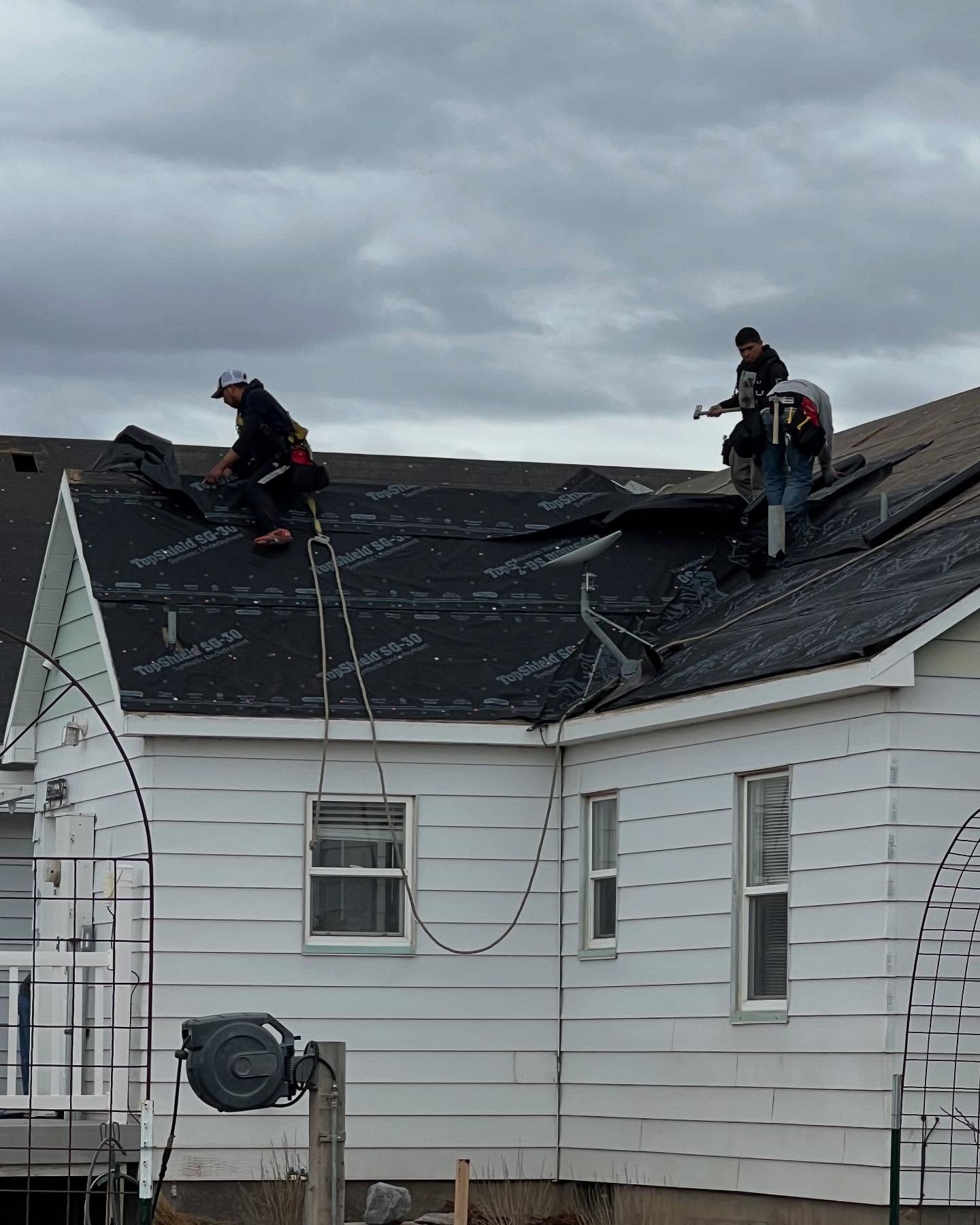 Roofers on a white house installing black roofing under cloudy skies