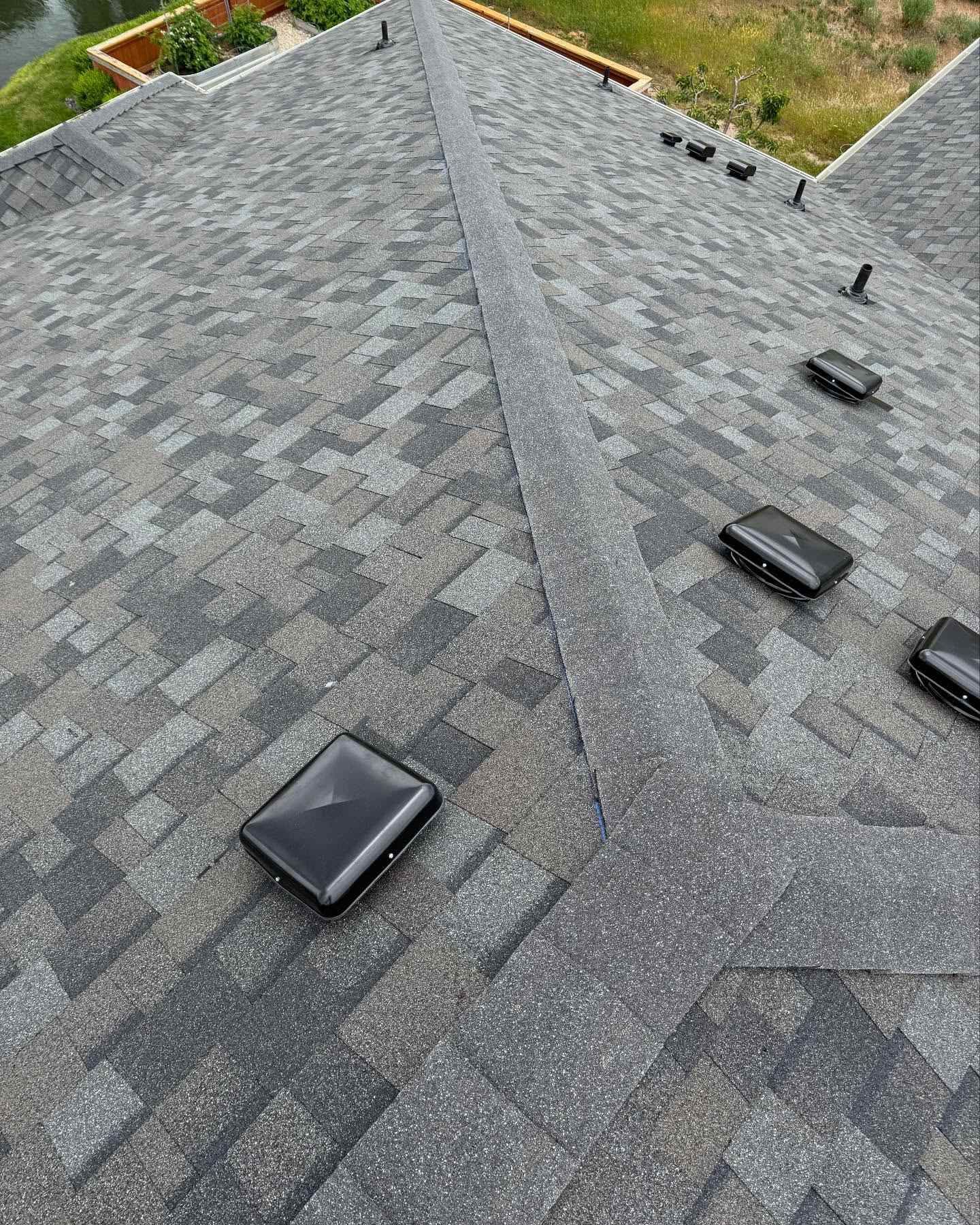 Aerial view of a gray shingled roof with several black vents and a few small solar panels.