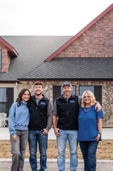 Four people standing outside a house, smiling in front of a brick and stone facade.