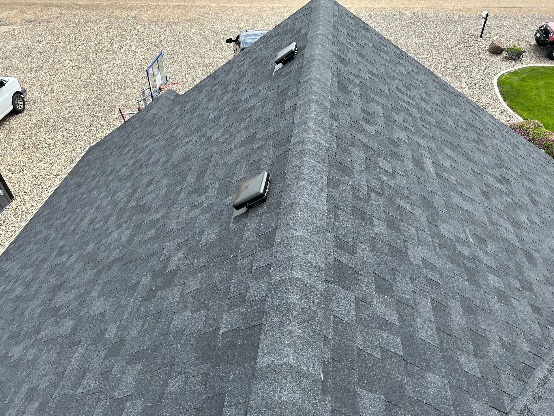 Aerial view of a dark gray shingled roof with two skylights and a gravel driveway below.