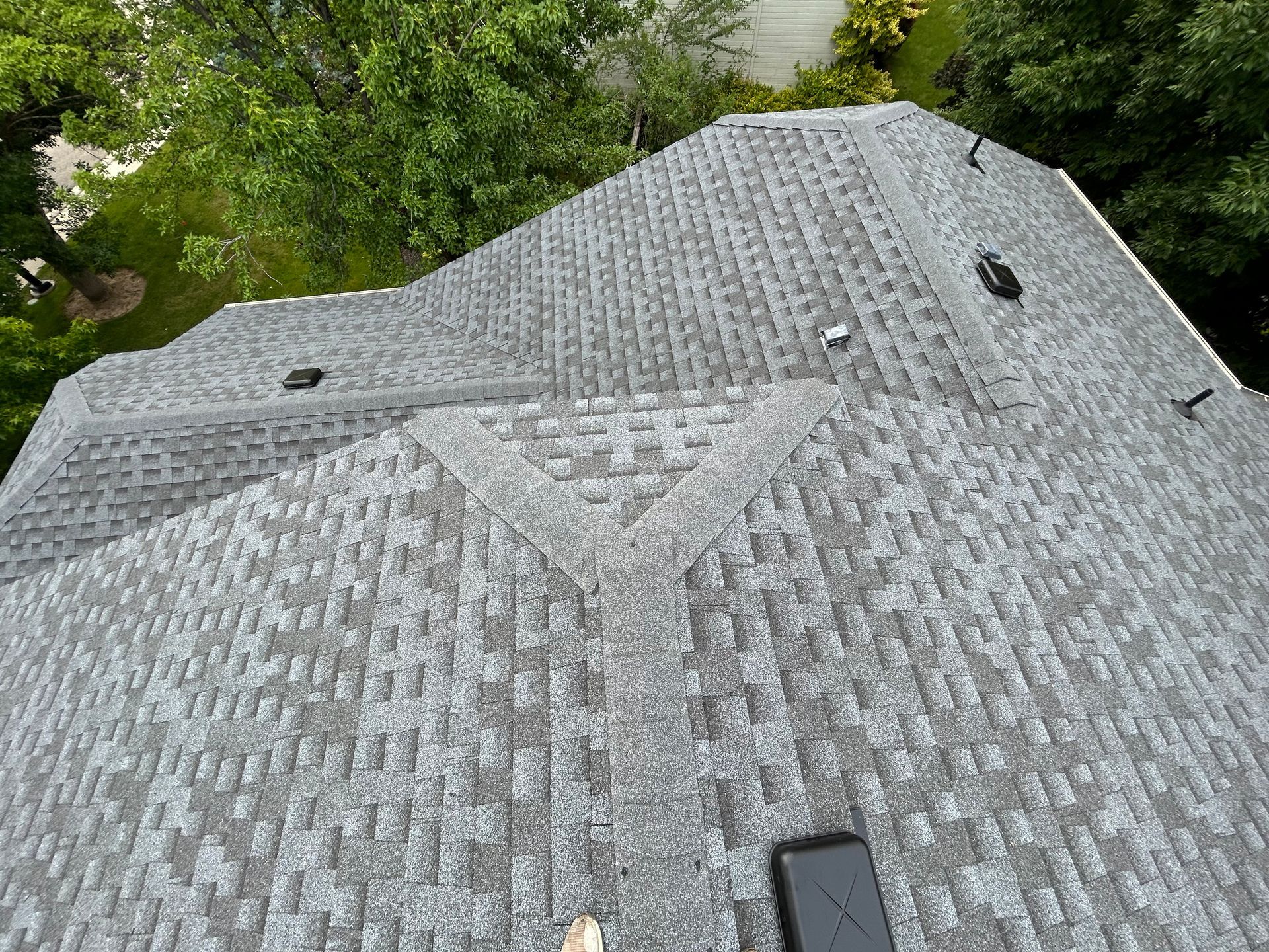 Gray shingled roof with vents, viewed from above, surrounded by green trees