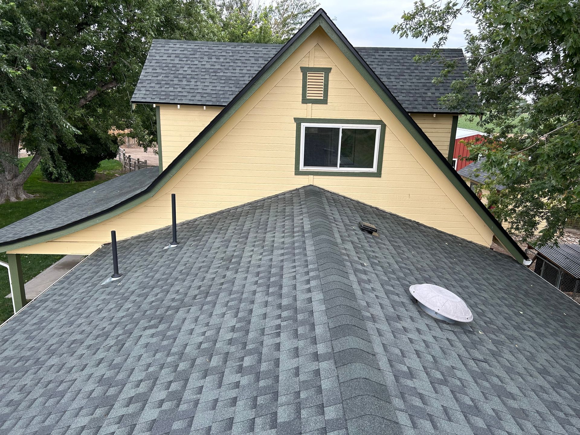 Gray shingled roof with skylight and vents, facing a yellow house with a black-framed window