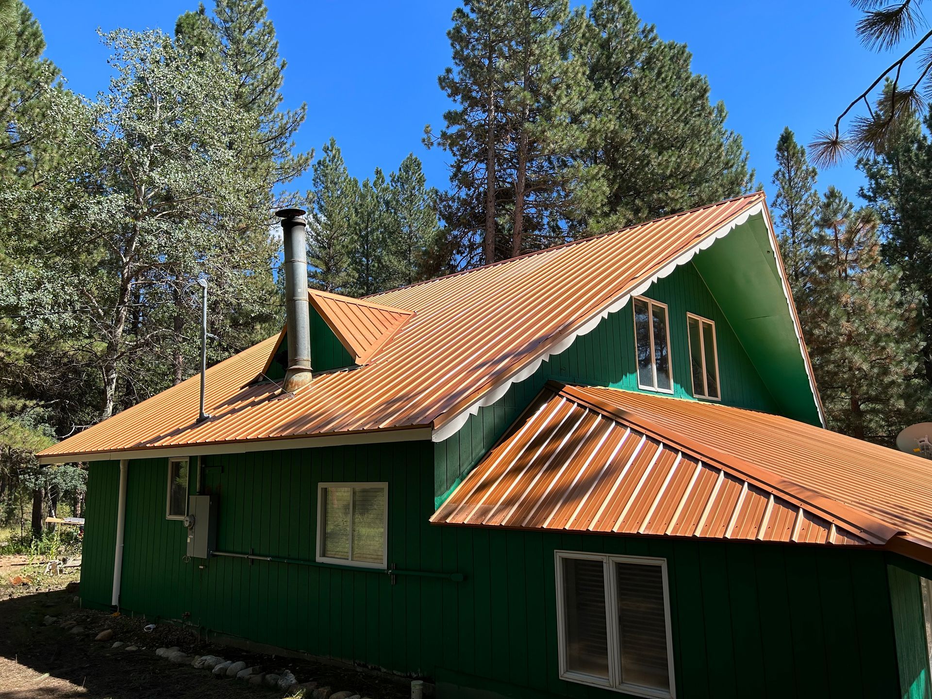 Green house with orange metal roof in a pine forest under a clear blue sky