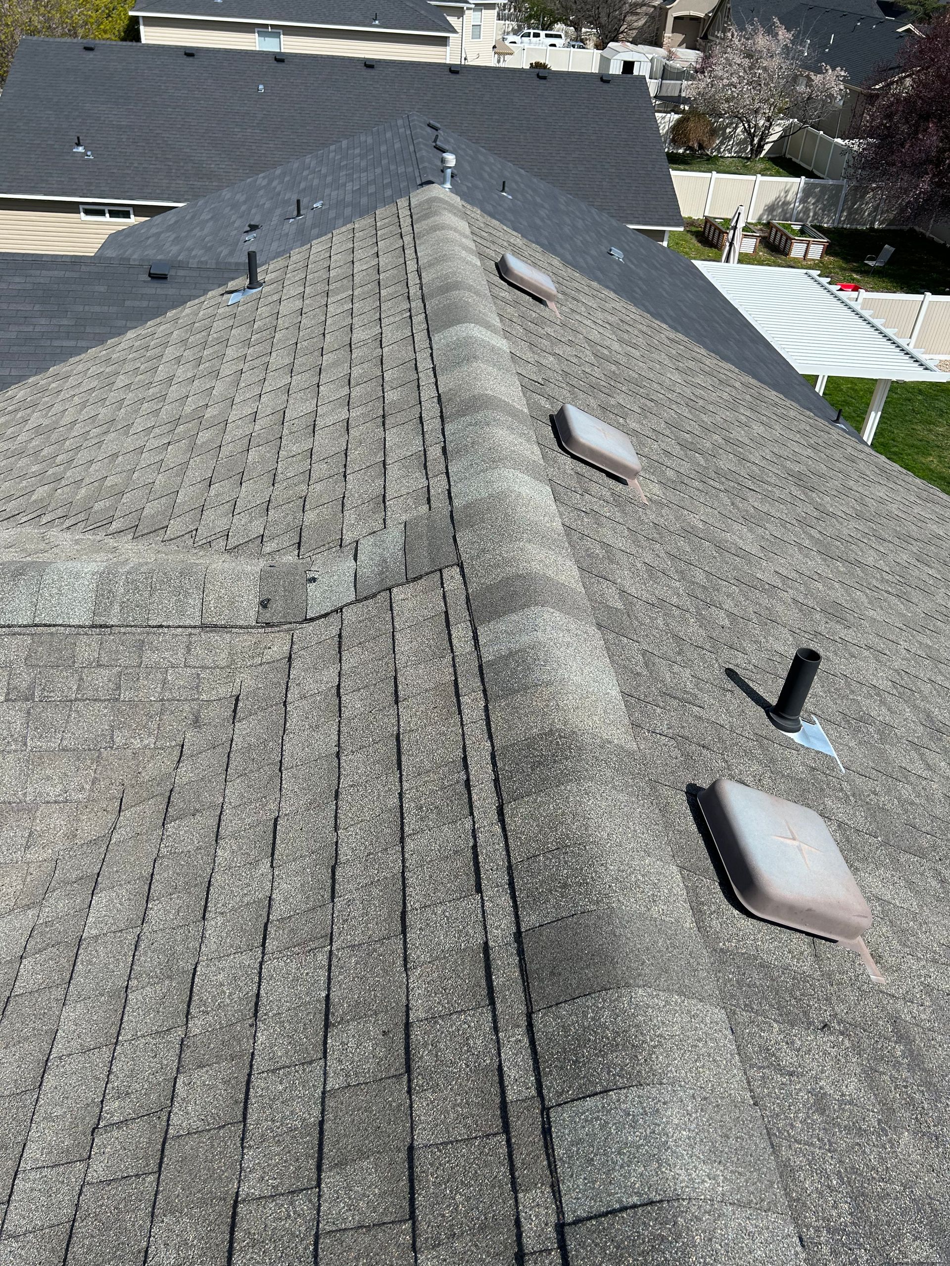 Close-up of a gray shingle roof ridge with vents and neighboring rooftops in view
