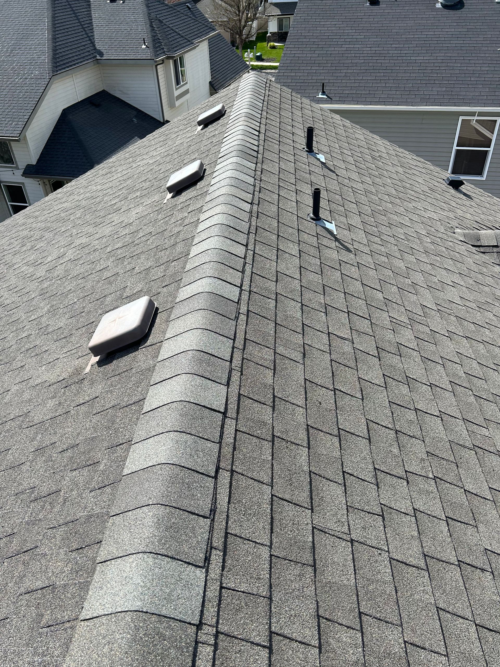 Rooftop with gray shingles and ridge vent, showing several roof vents on a sunny day
