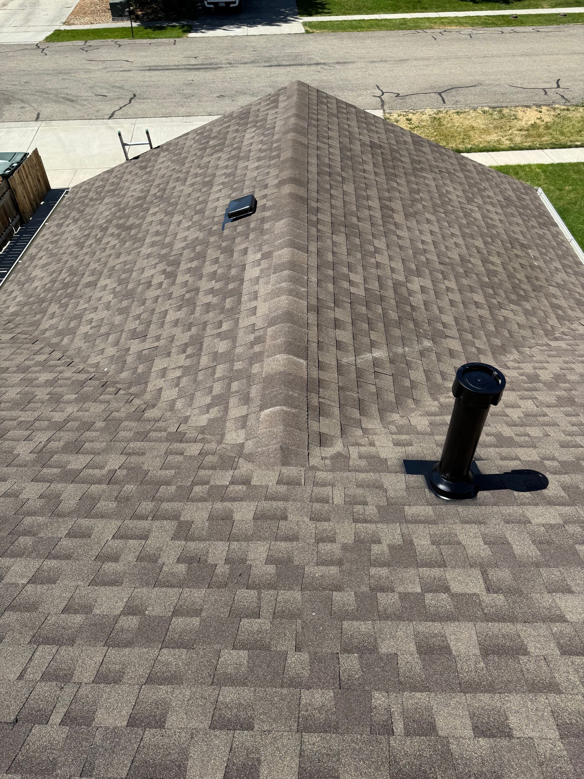 Gray shingle roof with a vent pipe and small roof opening near the ridge line