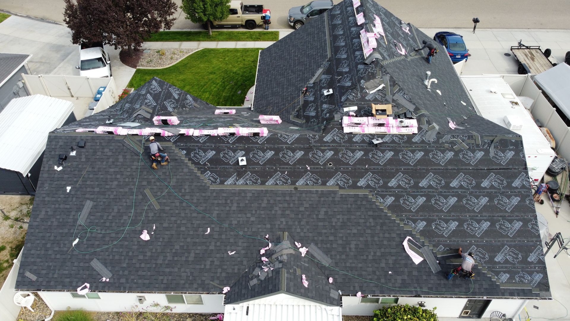 Aerial view of a house roof under repair, covered with black underlayment and scattered pink insulation.