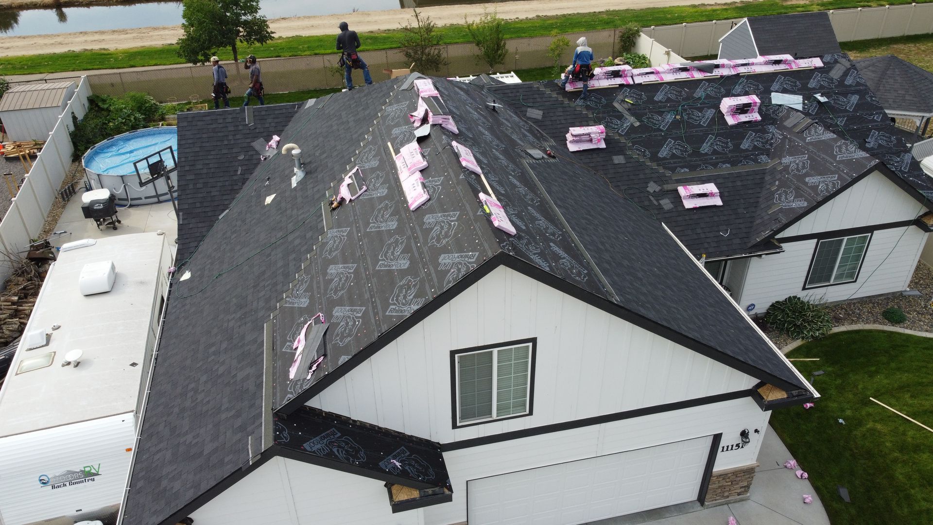 Aerial view of a house roof with storm damage and repair materials, with workers on the roof.