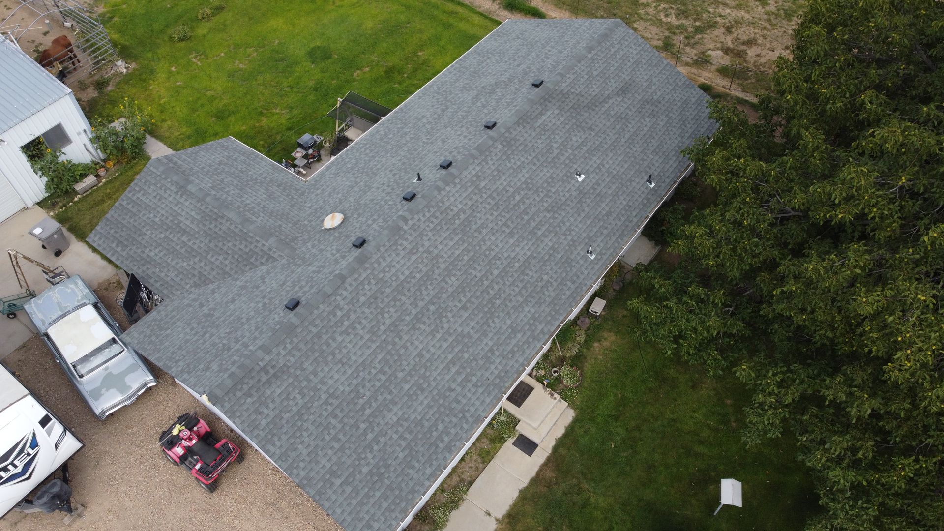 Aerial view of a gray-shingled house with a gravel driveway and trees around it.