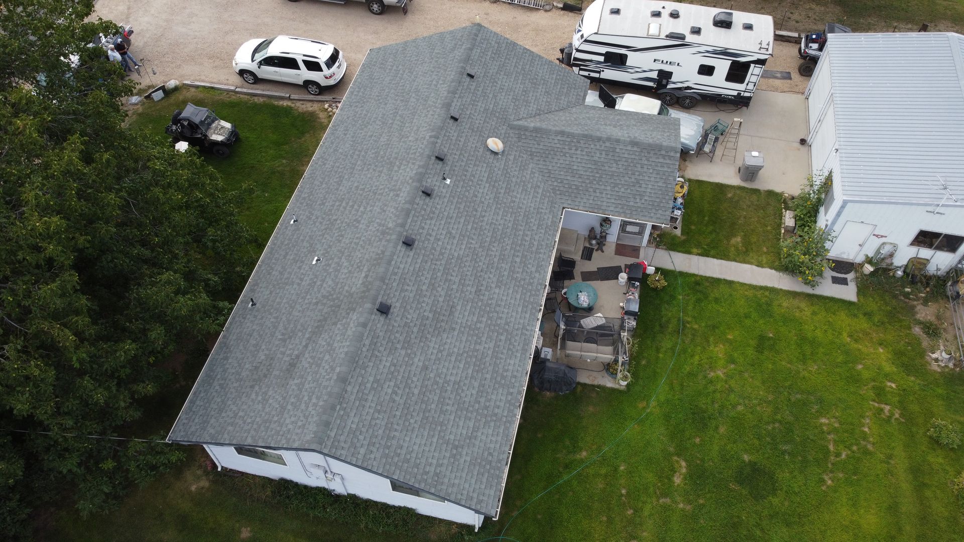 Aerial view of a gray-roofed house with vehicles parked in the driveway and a grassy yard.