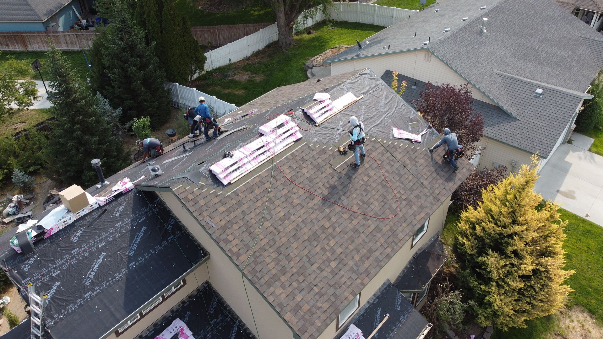 Workers on a roof installing shingles and roofing materials at a residential house.