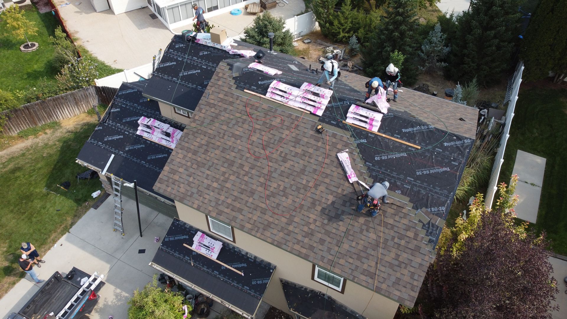 Aerial view of roofers installing pink underlayment on a house roof.