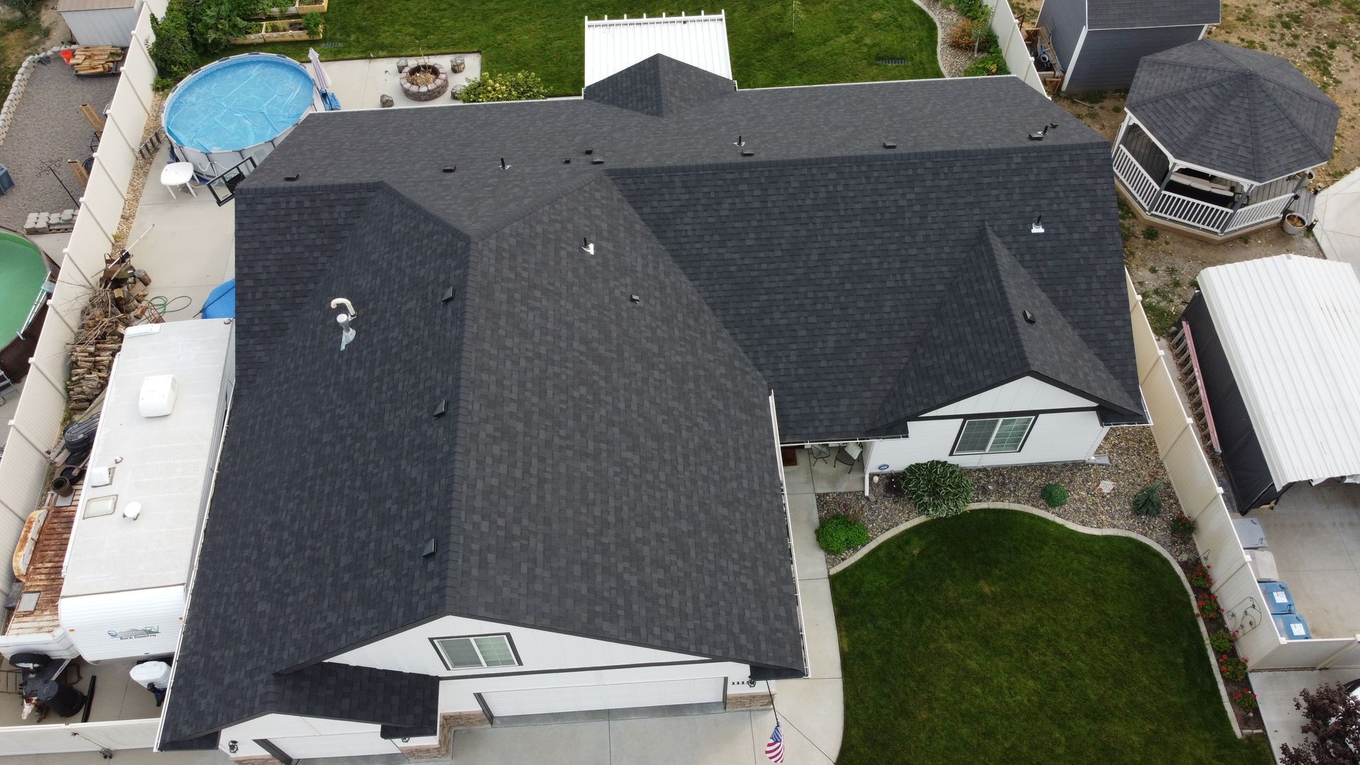 Aerial view of a house with a dark roof, backyard lawn, and a small above-ground pool