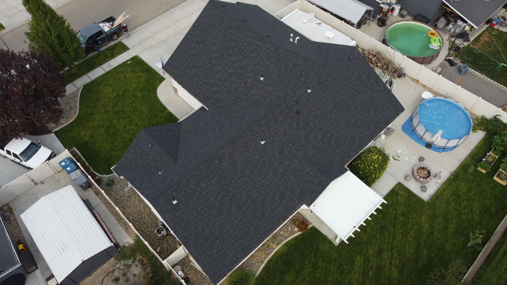 Aerial view of a house with a dark roof, backyard lawn, and above-ground blue pool.