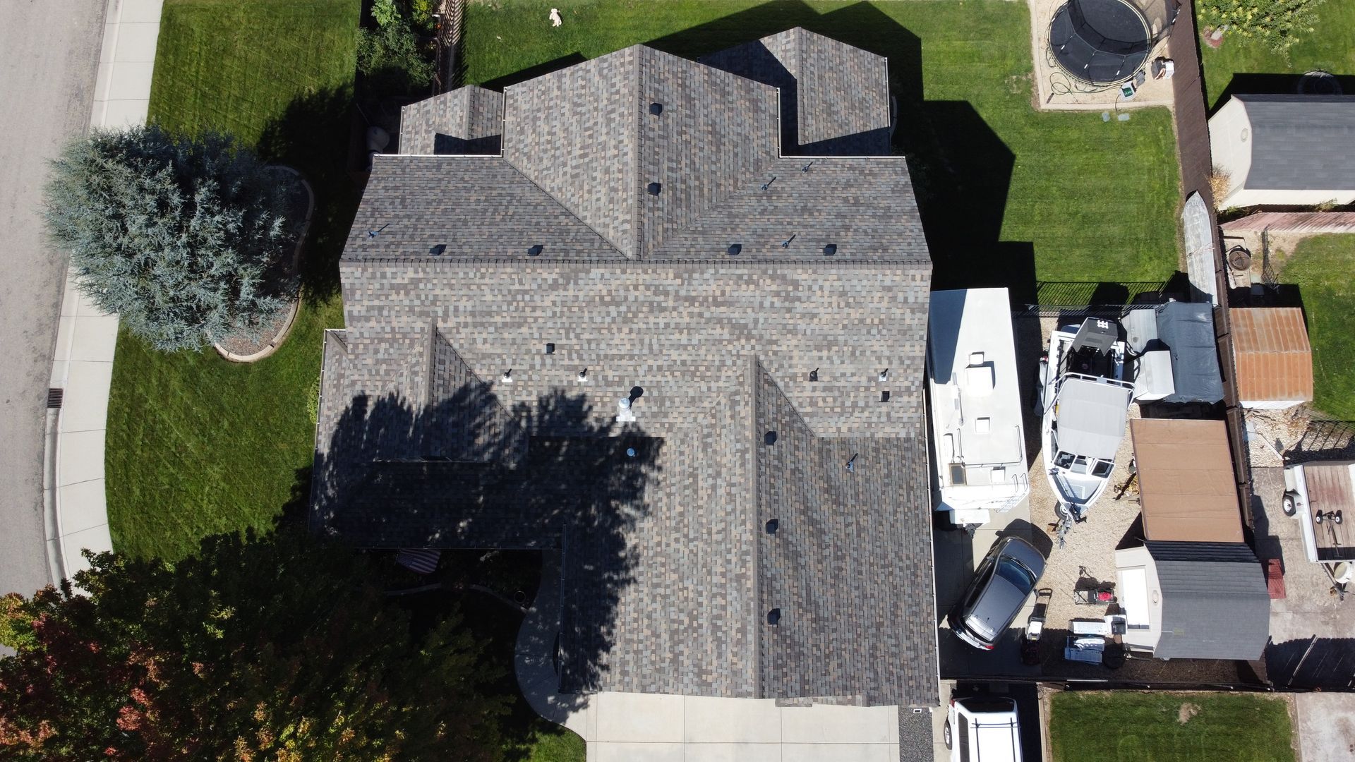 Aerial view of a gray-roofed house with trees, driveway, and parked vehicles beside it