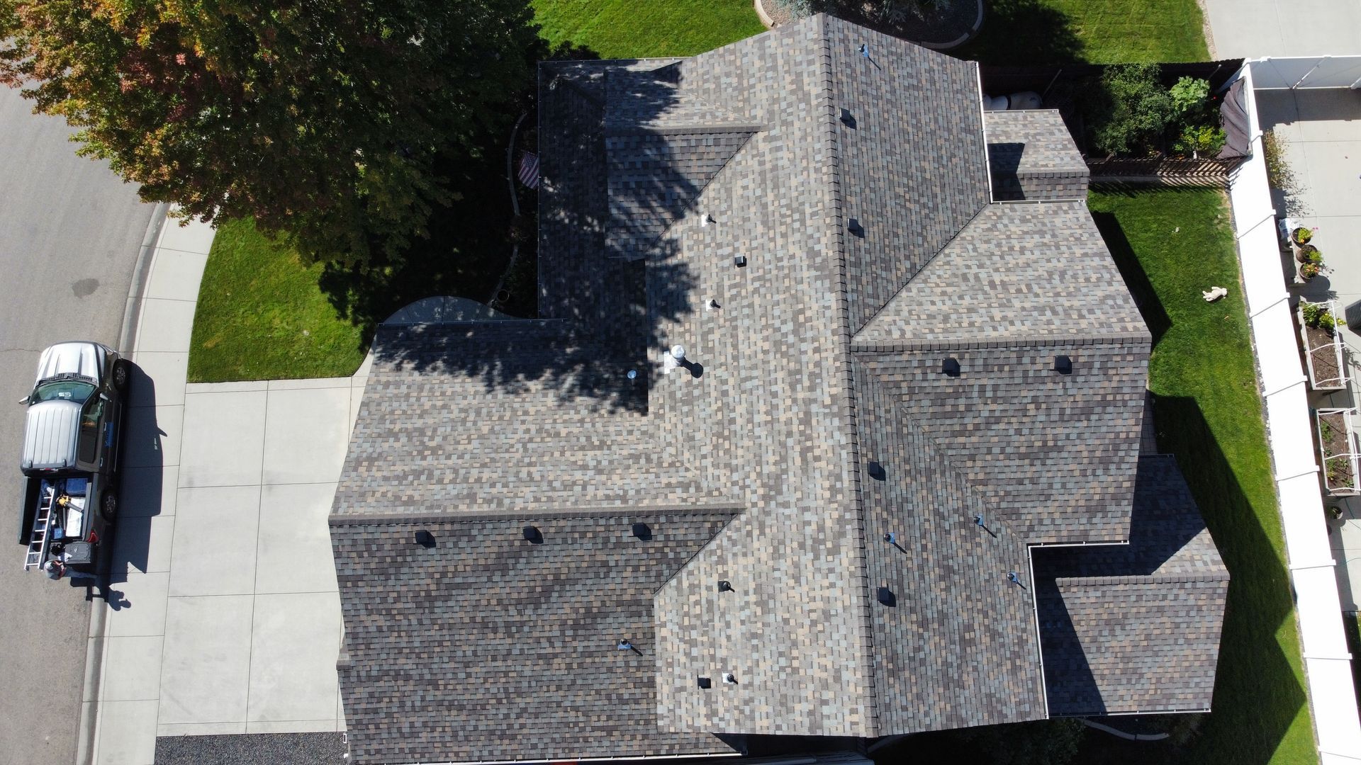 Aerial view of a gray-roofed house with driveway, lawn, and a parked car beside the street.