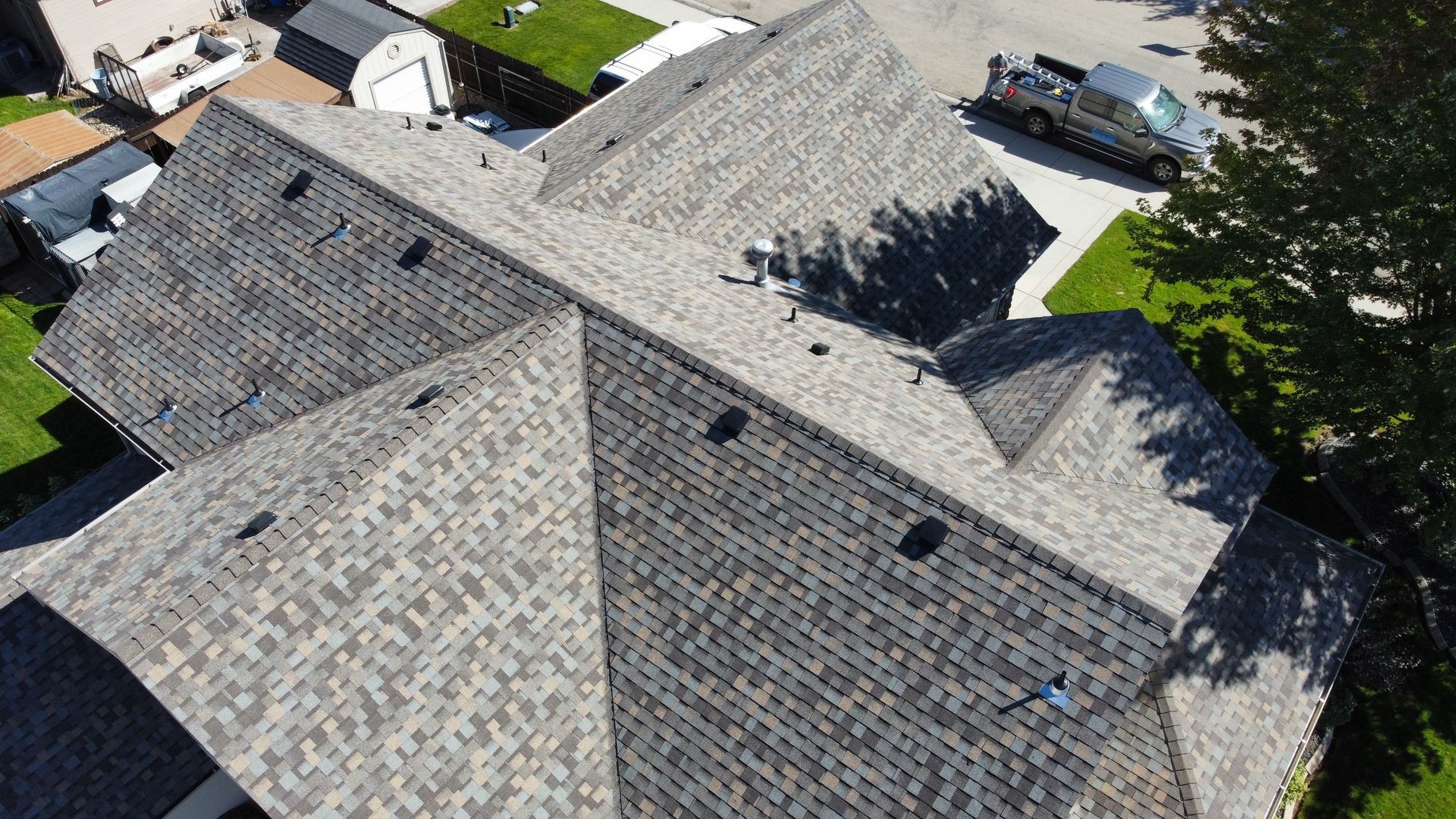 Aerial view of gray-shingled residential rooftops with parked cars and trees nearby