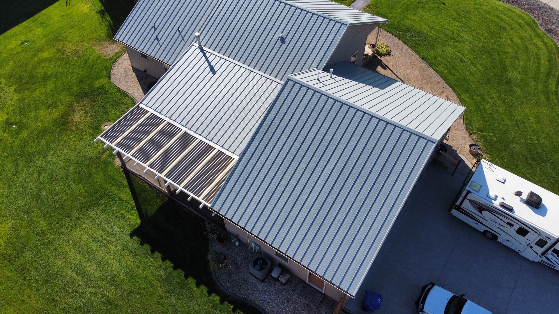 Aerial view of a house with gray metal roofs, skylights, and a small RV parked beside it.