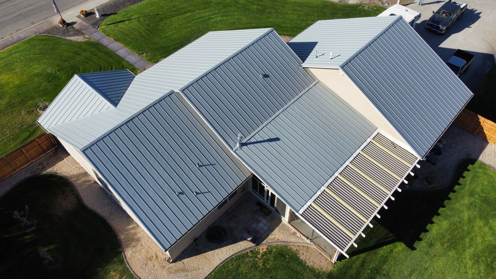 Aerial view of a large house with a gray metal roof and white trim on a grassy lot.