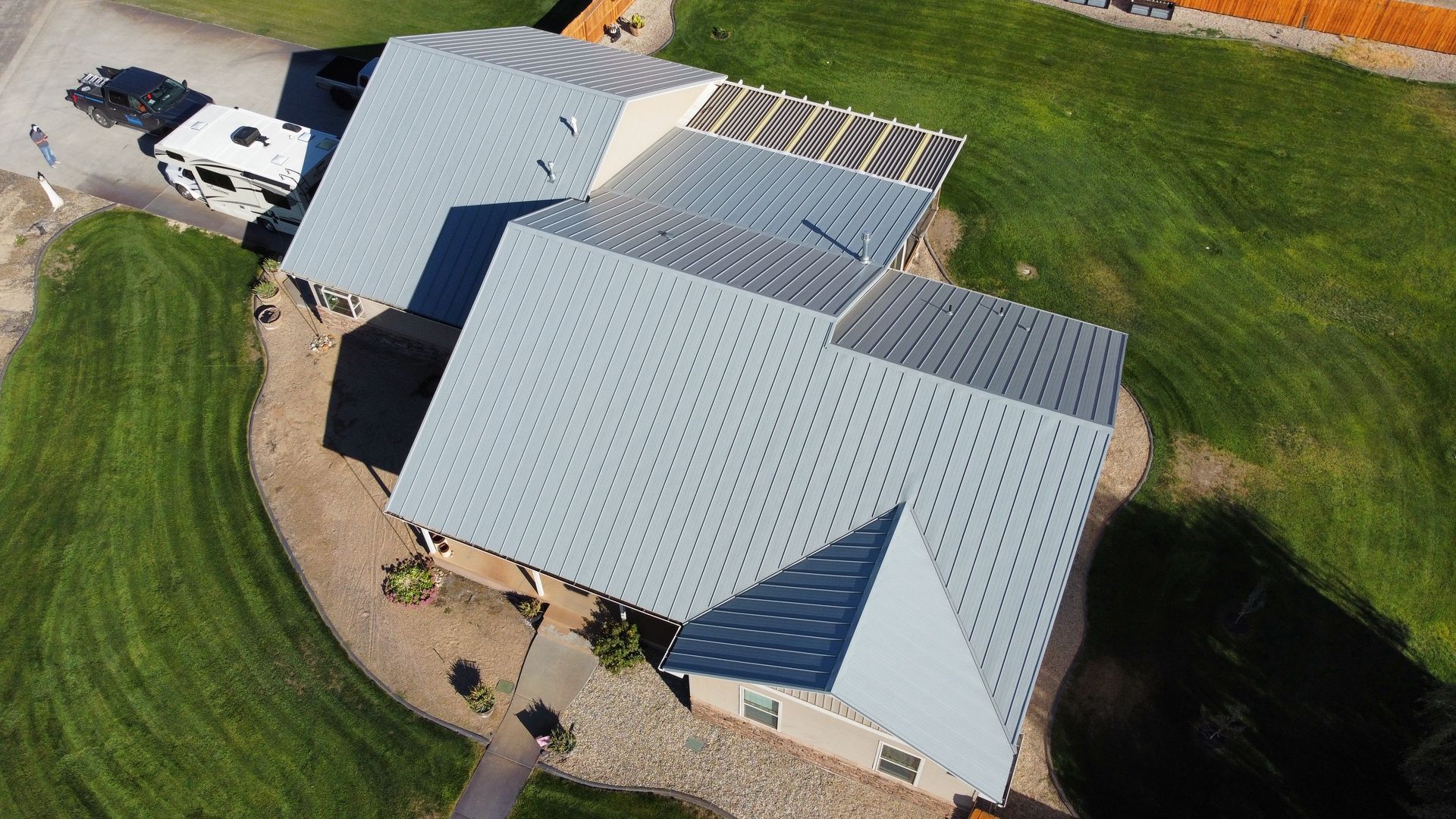 Aerial view of a house with a light gray roof, driveway, and green lawn on a sunny day