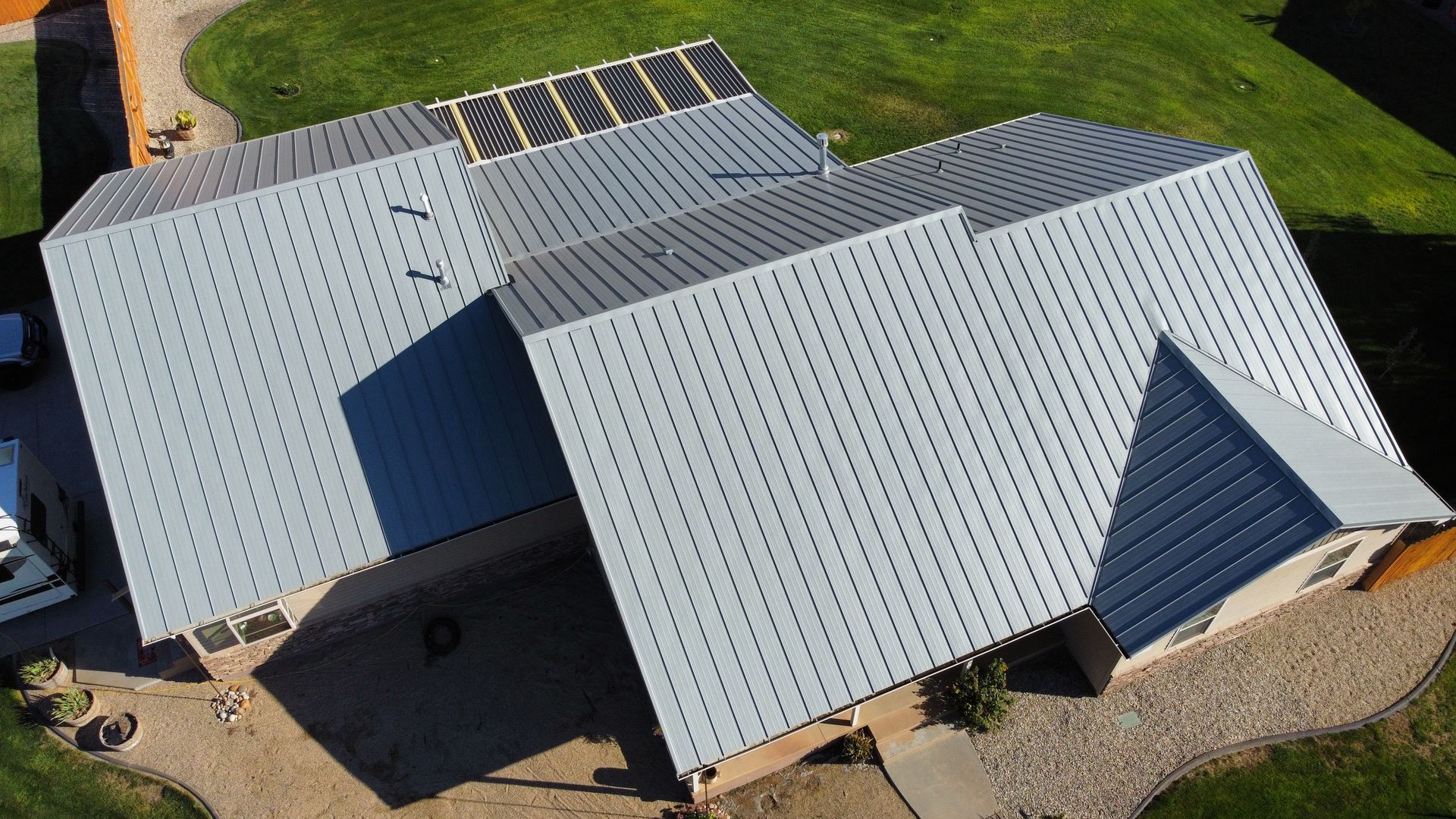 Aerial view of a house with a light gray metal roof and solar panels on one section.