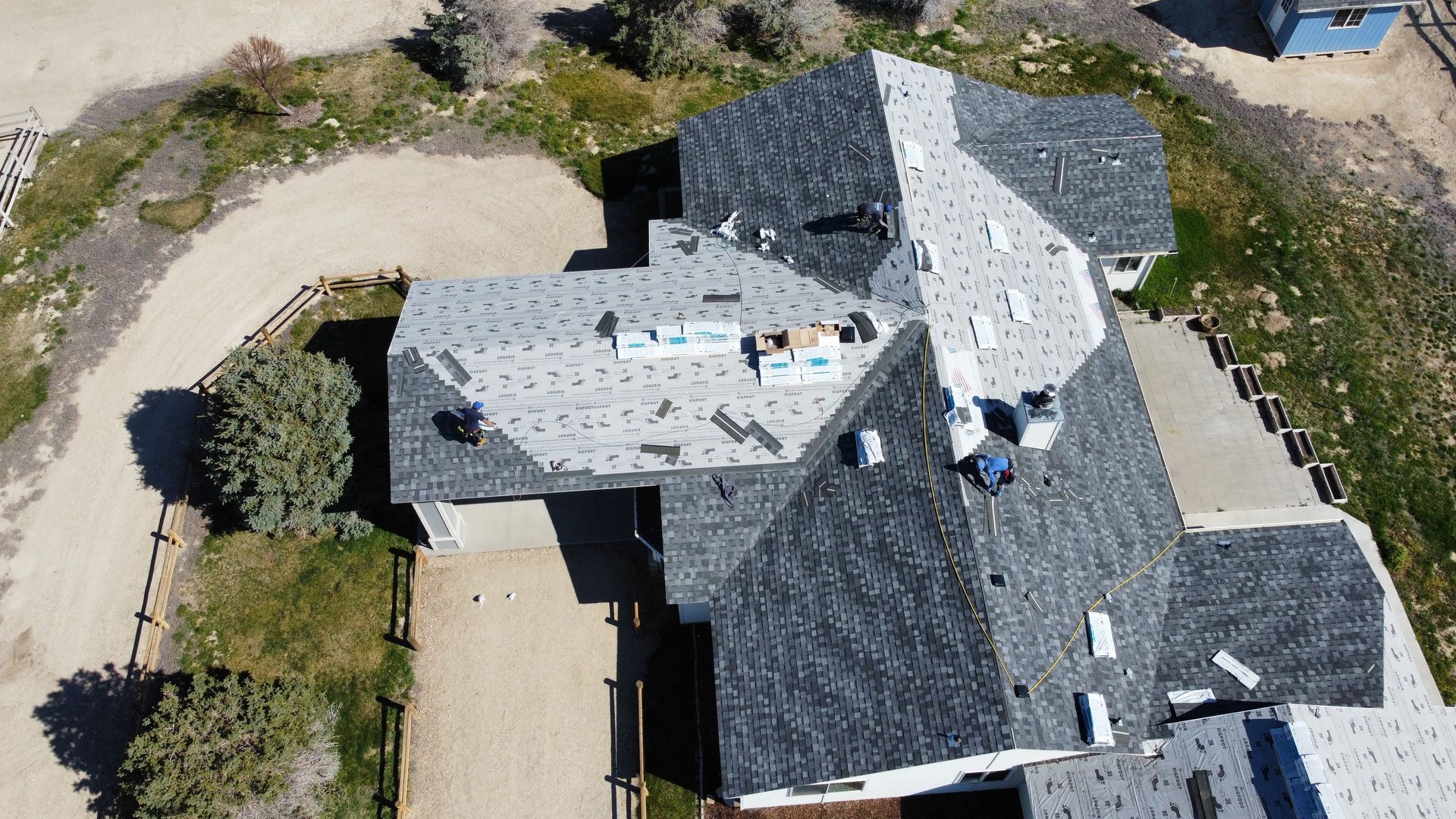 Aerial view of a gray-roofed house with workers on the roof and a curved driveway beside it