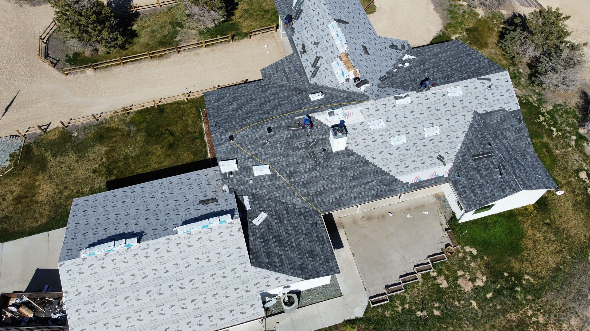Aerial view of a house with gray shingle roof, attached garage, and driveway surrounded by grass.