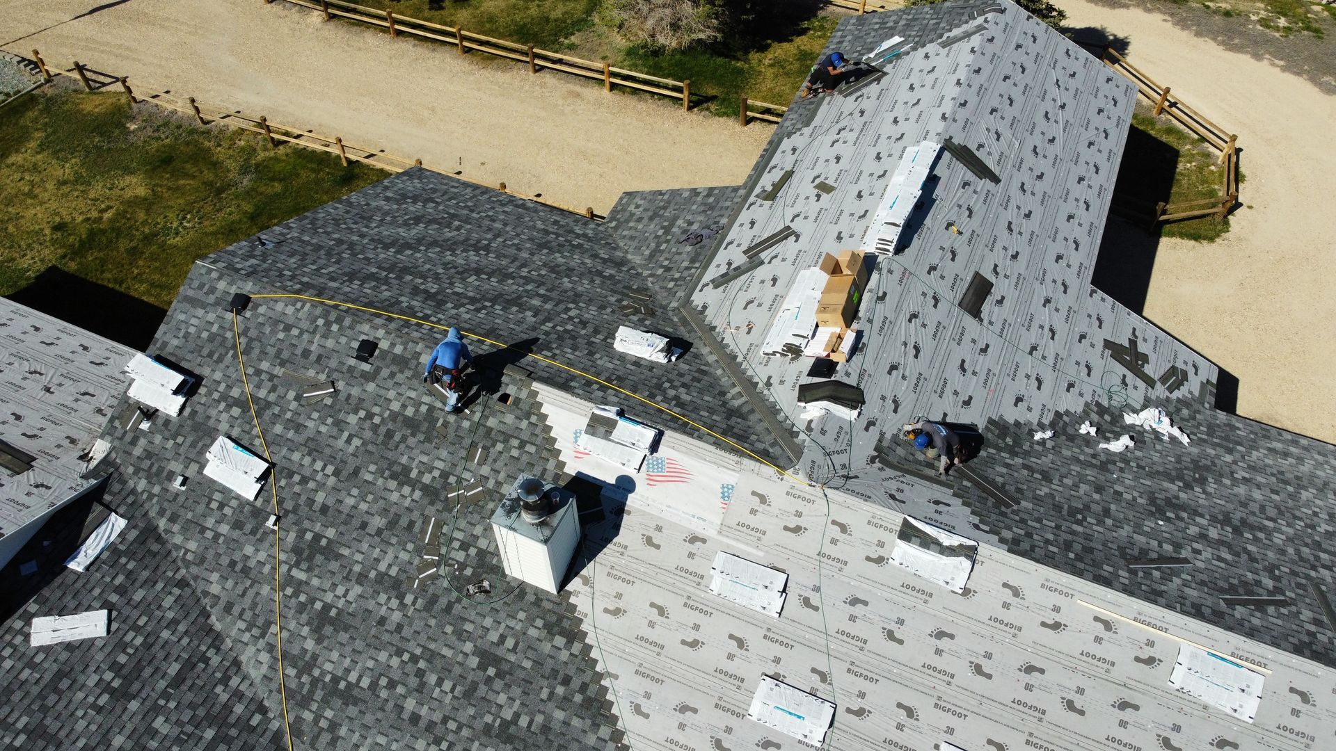 Roofers working on a gray shingled house roof during installation/repair