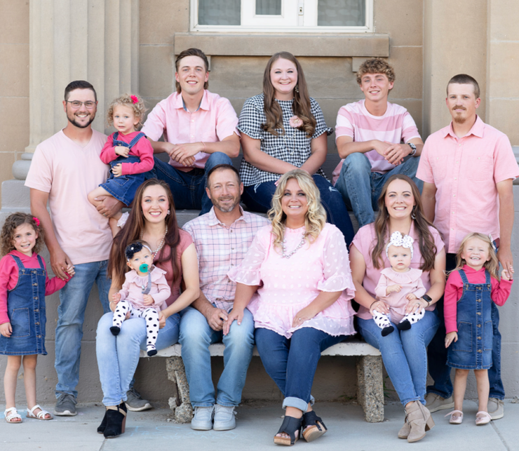 Large family group posing on porch steps, seated and standing together in casual pink and denim outfits.