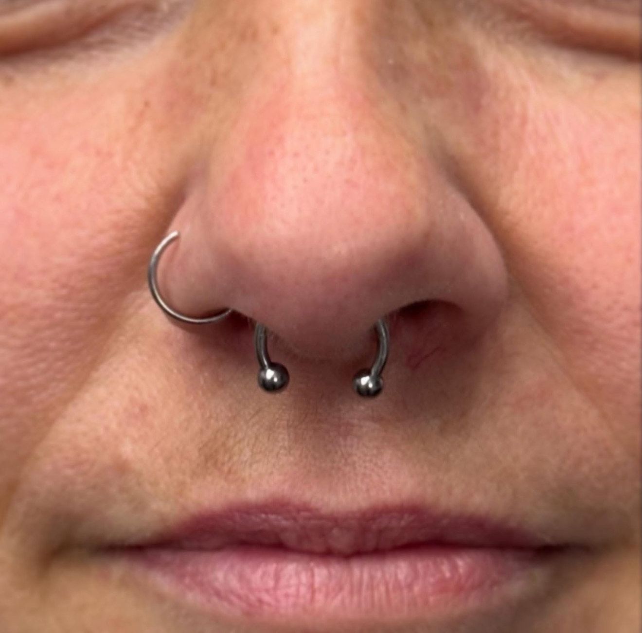 Close-up of a person's nose with a septum piercing and nostril piercing, silver jewelry.