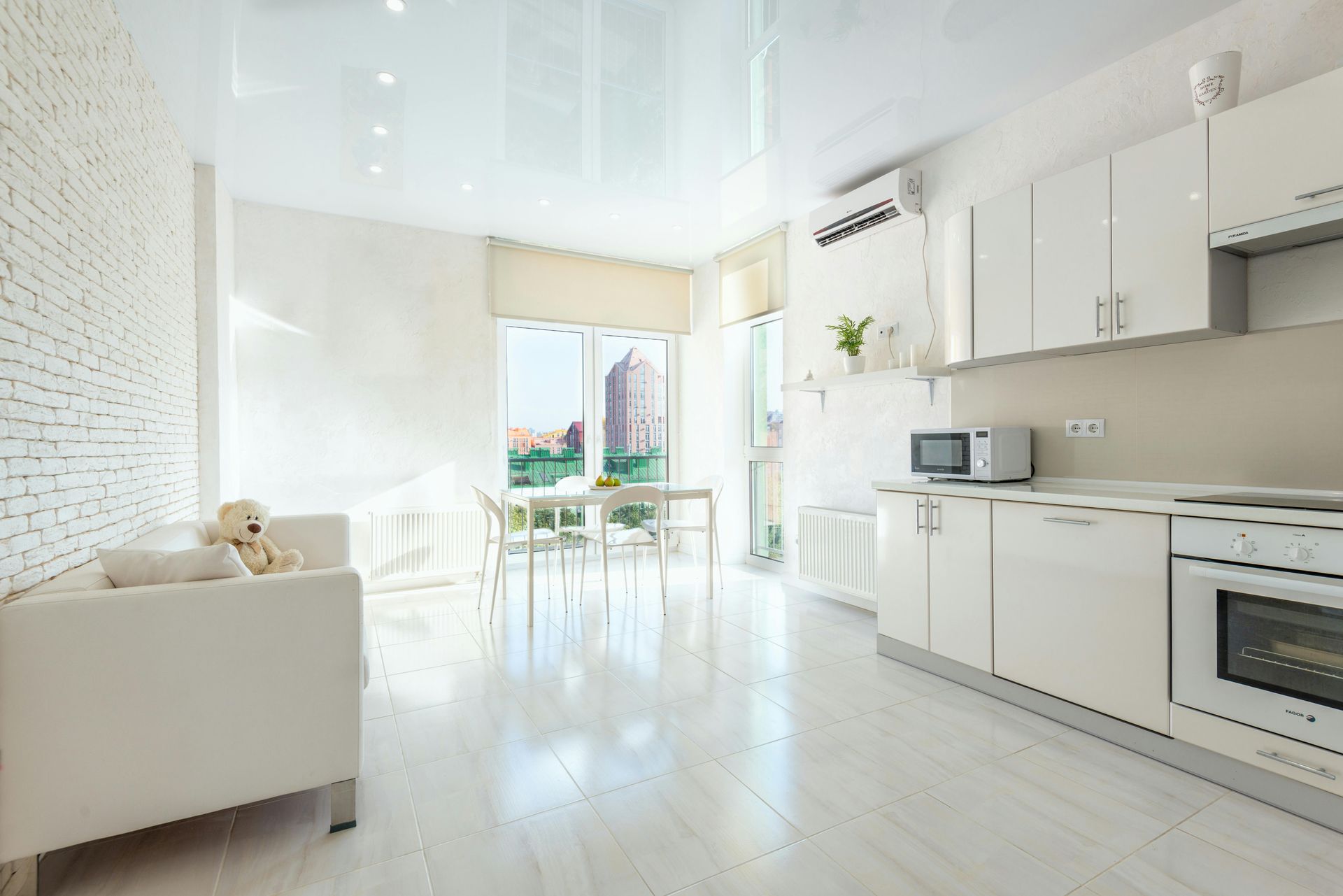 Bright modern kitchen and living room with white cabinets, sofa, and open balcony doors