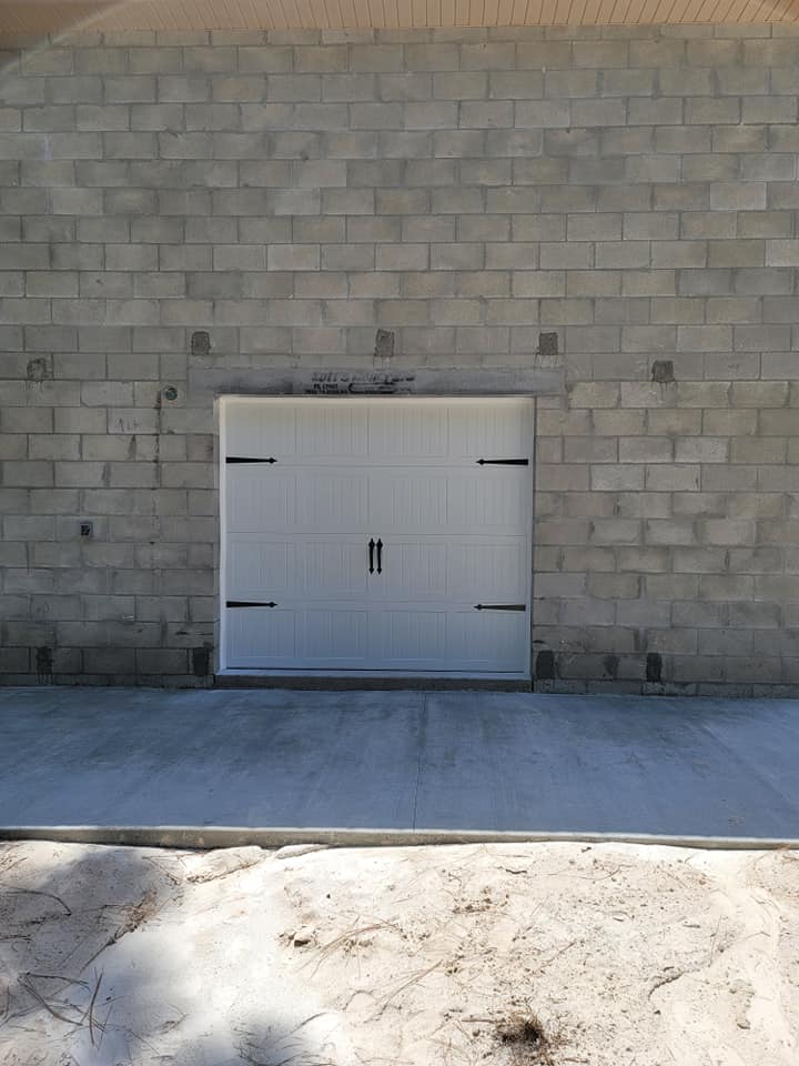 A white garage door is against a brick wall