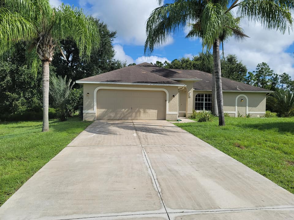 A house with a driveway and garage door has palm trees in front of it.