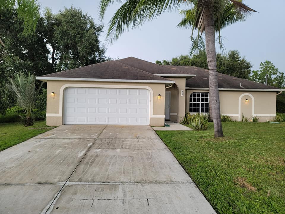 A house with a garage door and palm trees in front of it. 